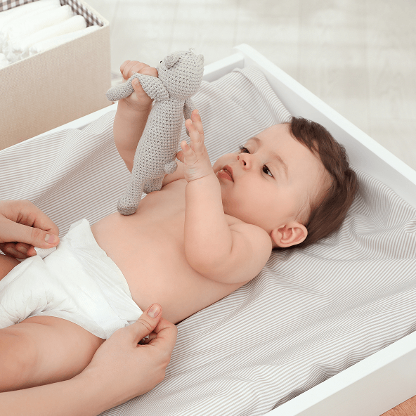 Mały bobas w pampersie z misiem w rękach, leżący na przewijaku.