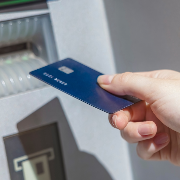 Zbliżenie na granatową kartę płatniczą, którą ktoś trzyma w prawym ręku w próbuje włożyć do bankomatu w M1 Kraków.