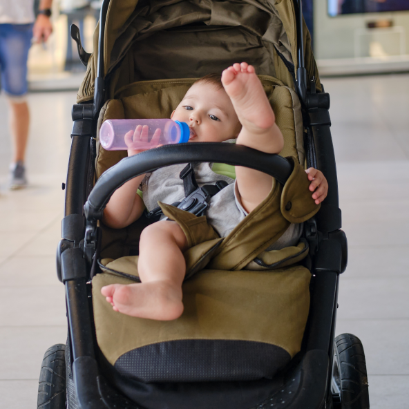 Dziecko w wózku pije z butelki i unosi nogę w górę