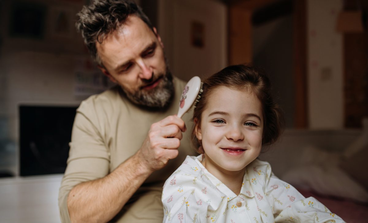 Obraz przedstawiający uśmiechniętego ojca robiącego fryzurę swojemu dziecdu