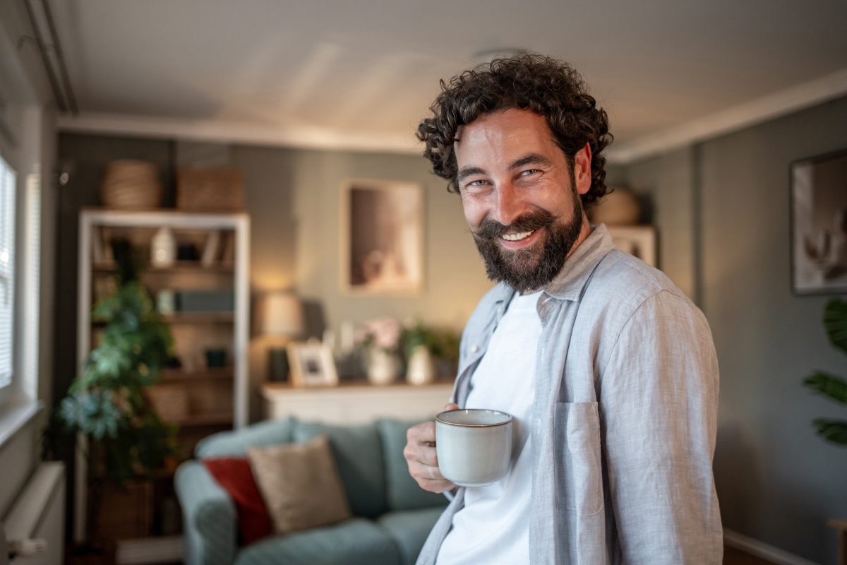 Obraz przedstawiający uśmiechniętego mężczyznę z kubkiem gorącej kawy