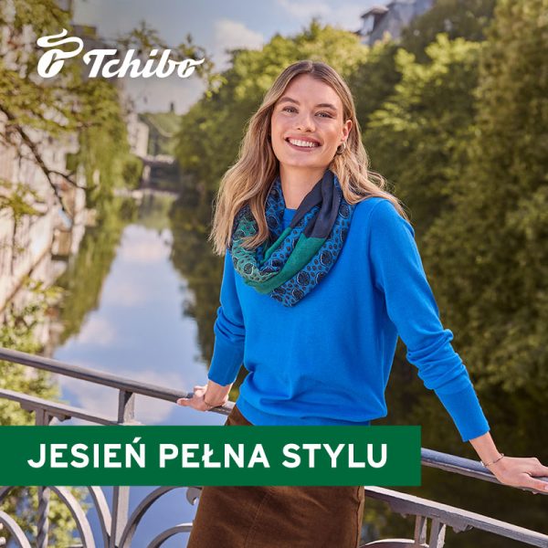 Grafika promocyjna marki Tchibo. Blondynka w niebieskim sweterku stojąca na moście nad rzeką w słoneczny dzień.